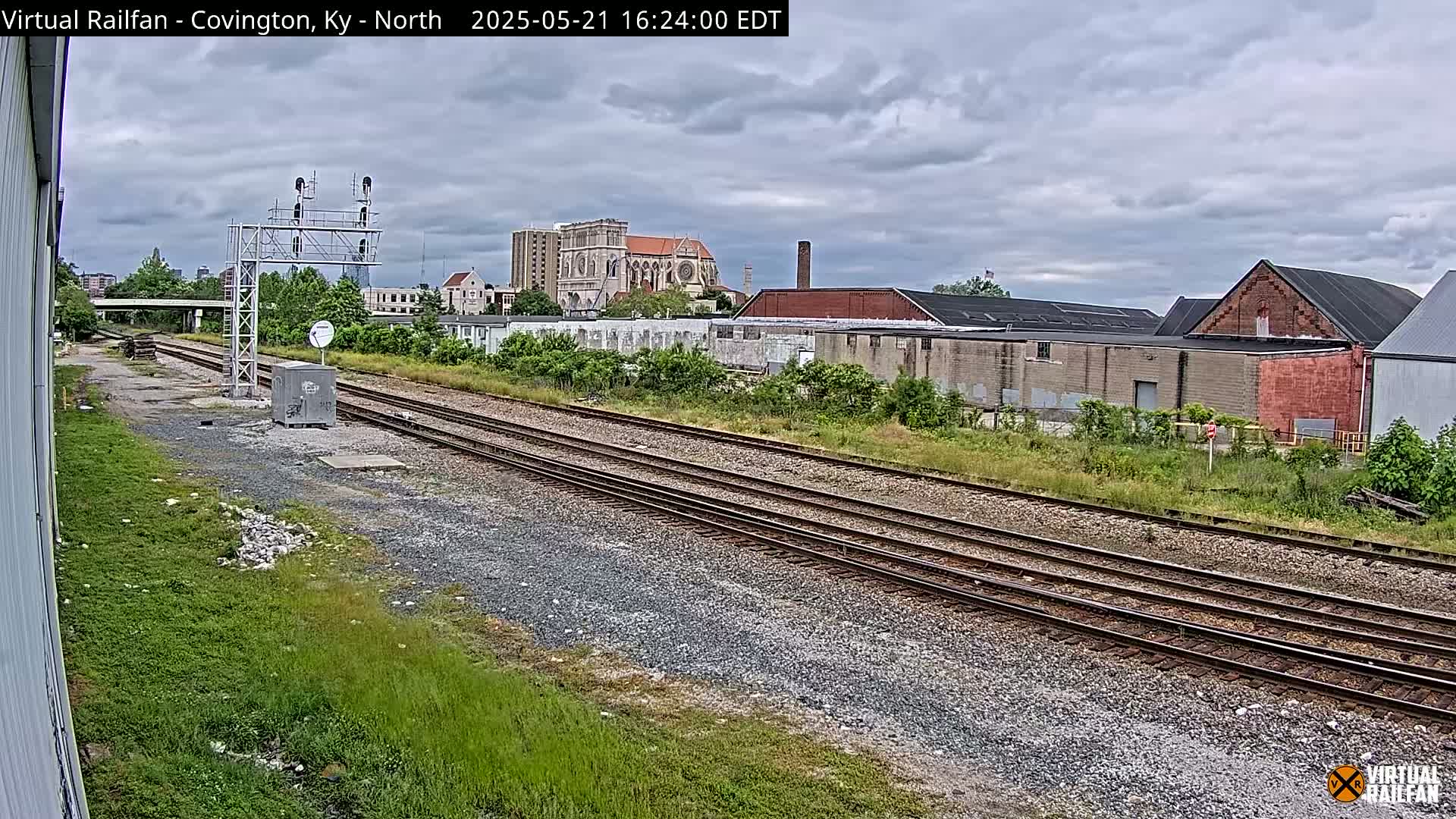 Railroad tracks extend into the distance under an overcast sky, past industrial buildings and a large church in the background.