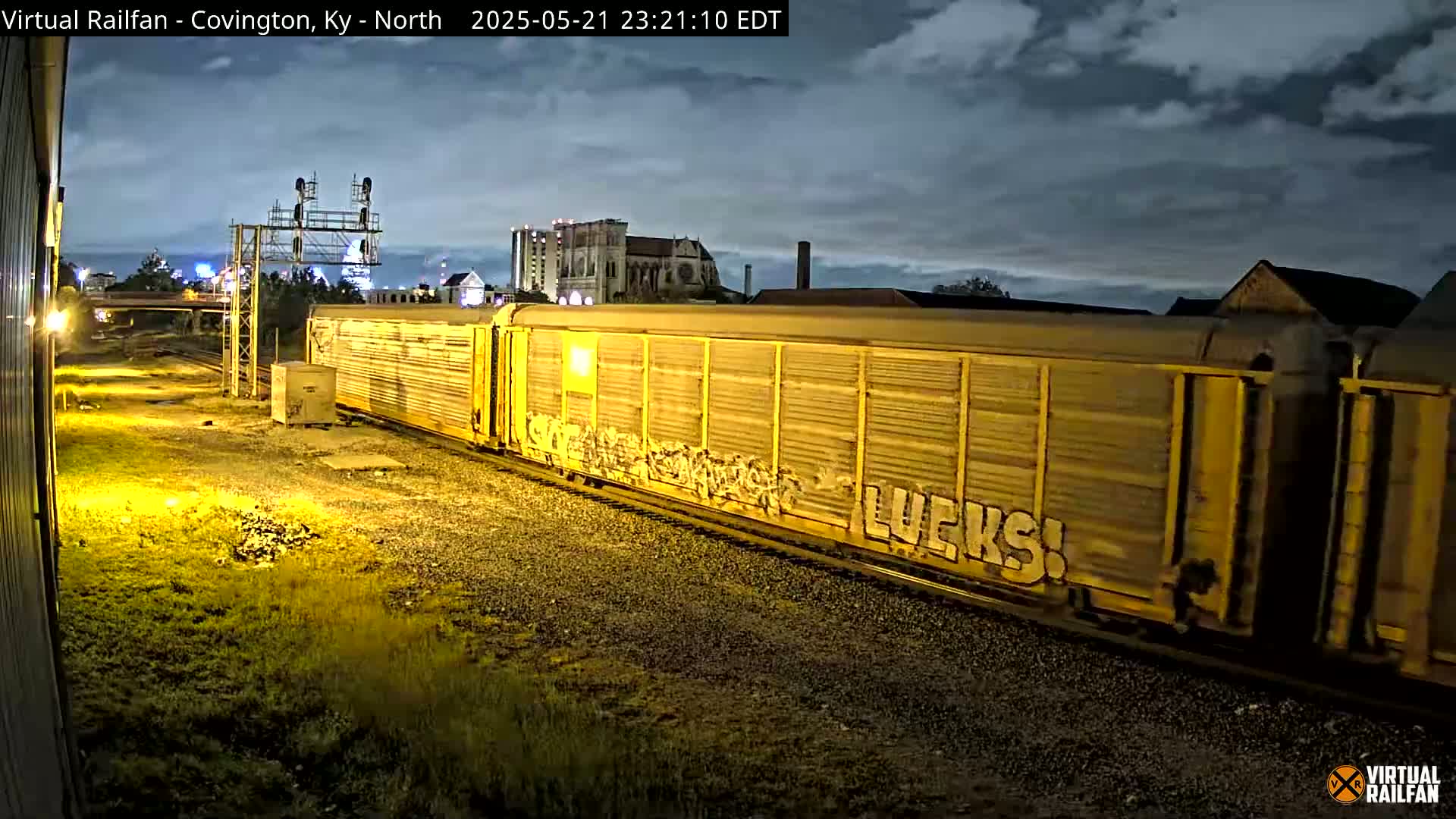 A long yellow freight train with graffiti passes by at night under a partly cloudy sky.