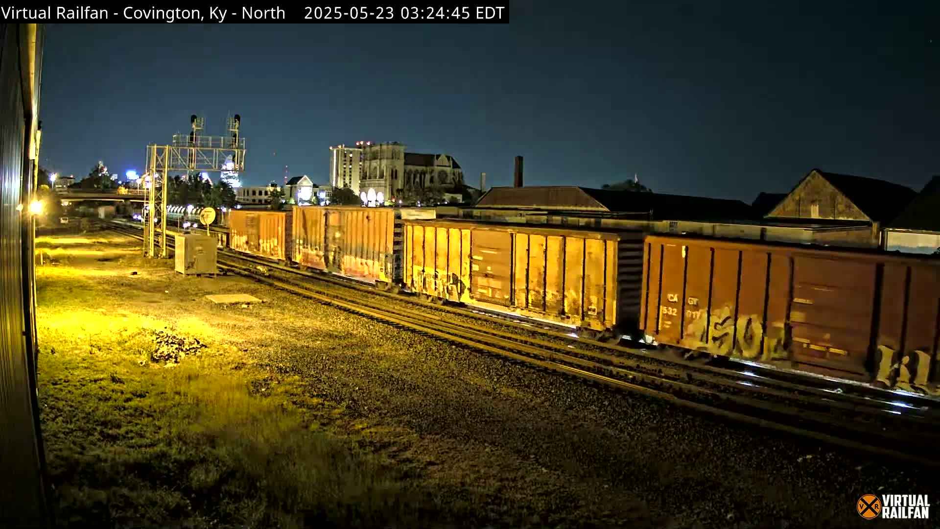 A long freight train with graffiti-covered cars moves along railroad tracks at night under a clear, dark sky.