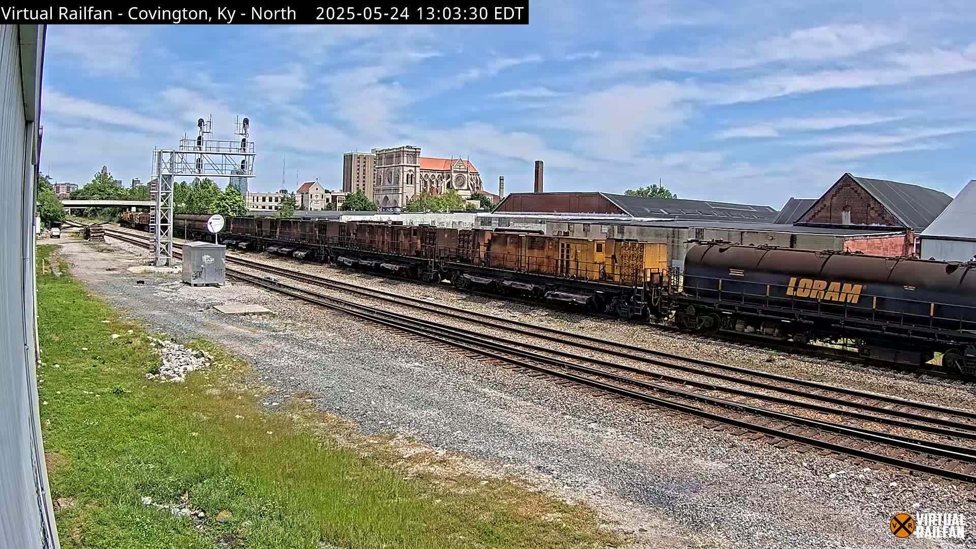 A long freight train sits on parallel train tracks under a partly cloudy sky.