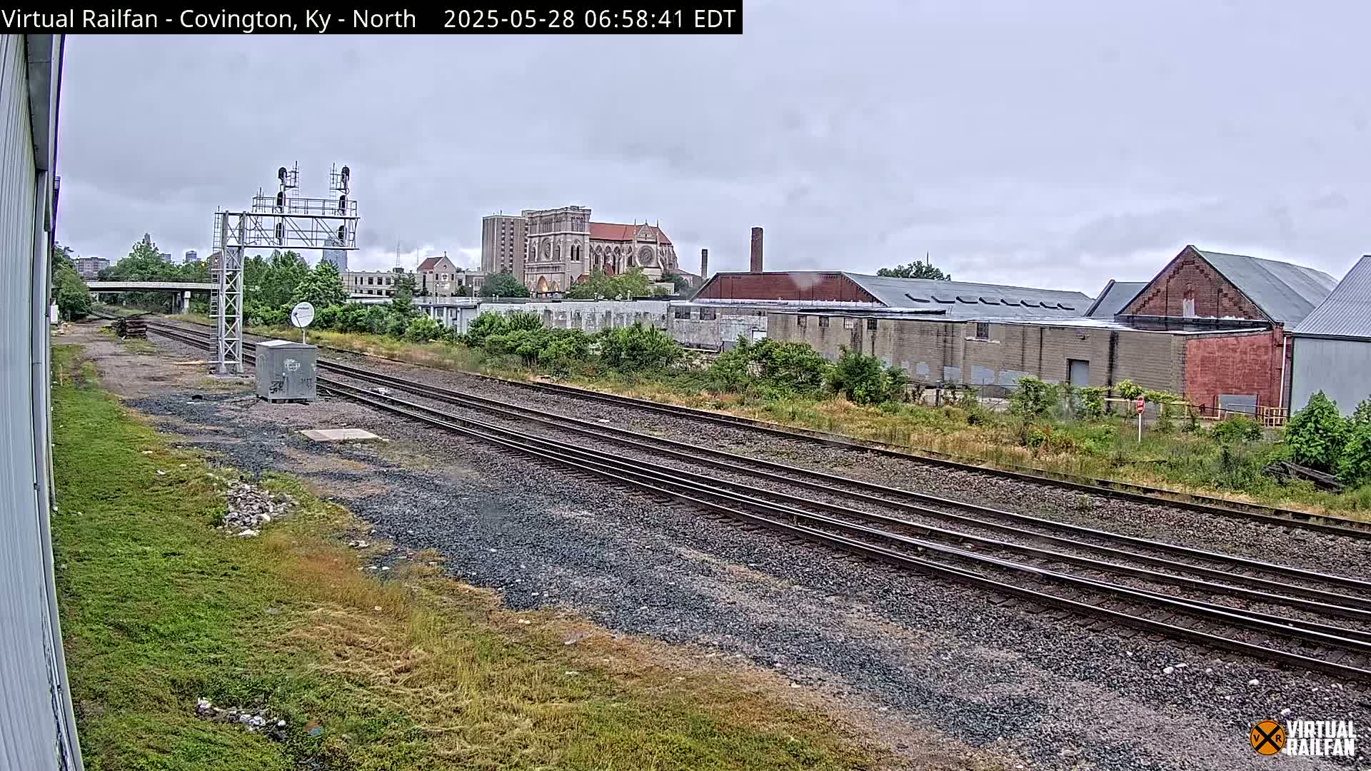 Multiple train tracks run through a grassy area toward a cityscape under an overcast sky.