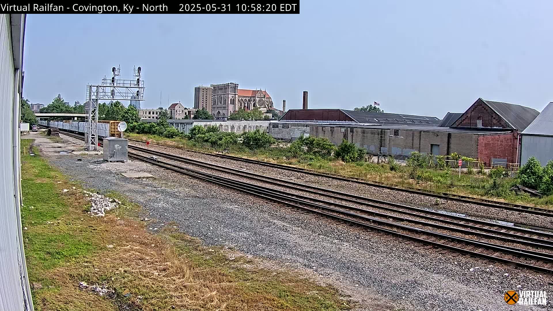 A train sits on railroad tracks next to industrial buildings under a clear sky.