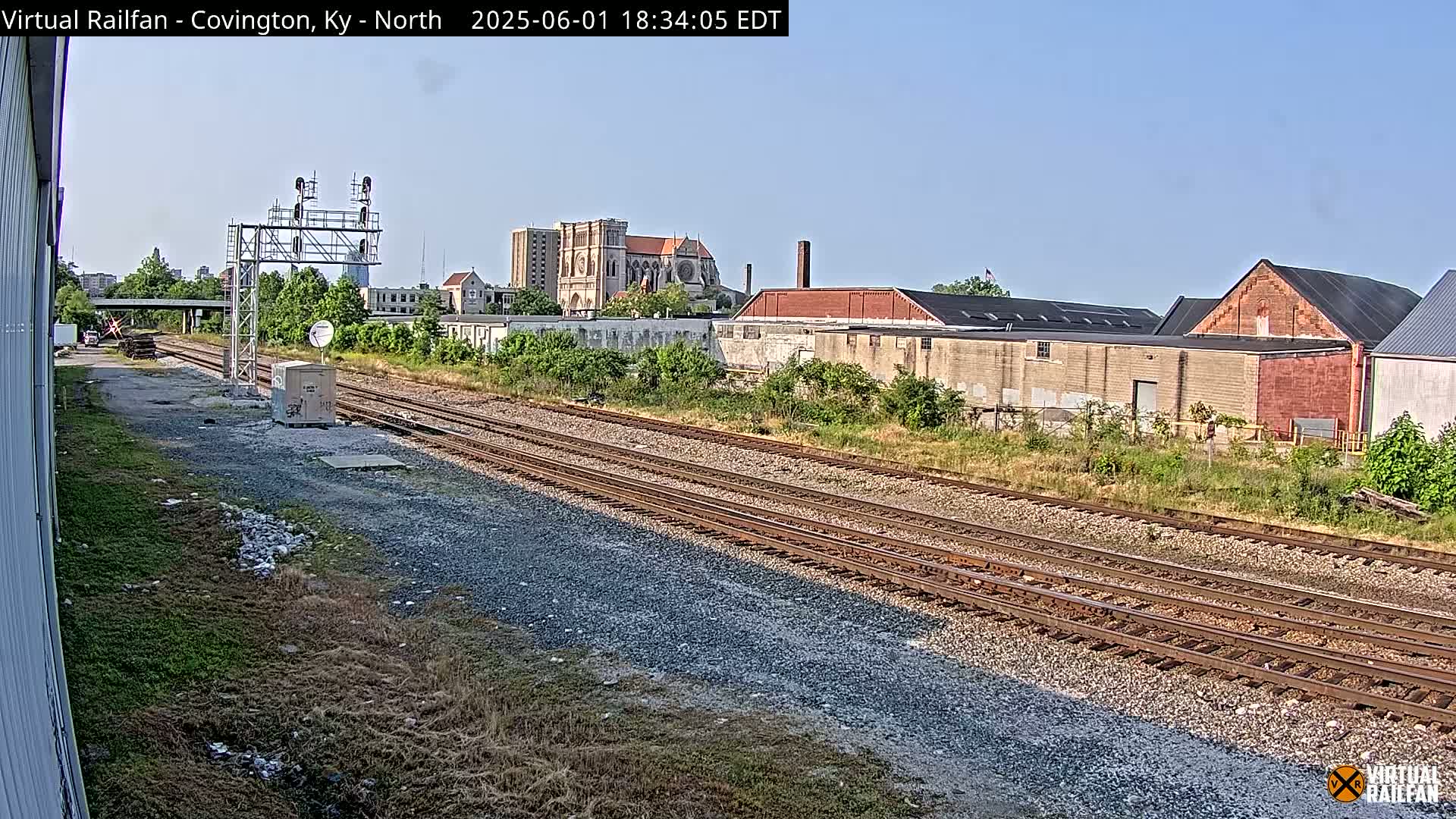 A view of railroad tracks on a sunny day, with industrial buildings and a large church in the background.