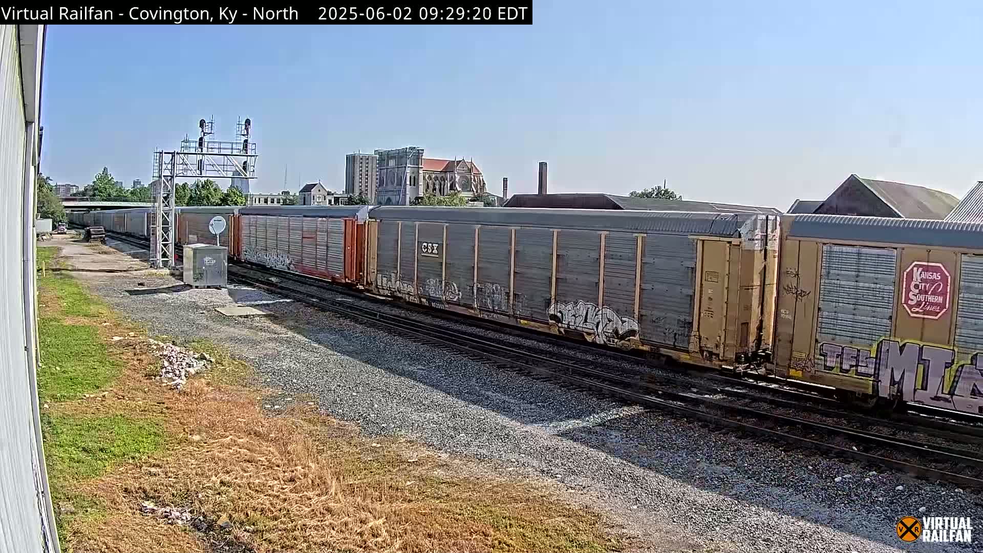 A long freight train with graffiti on some cars sits on a railway track under a clear blue sky.