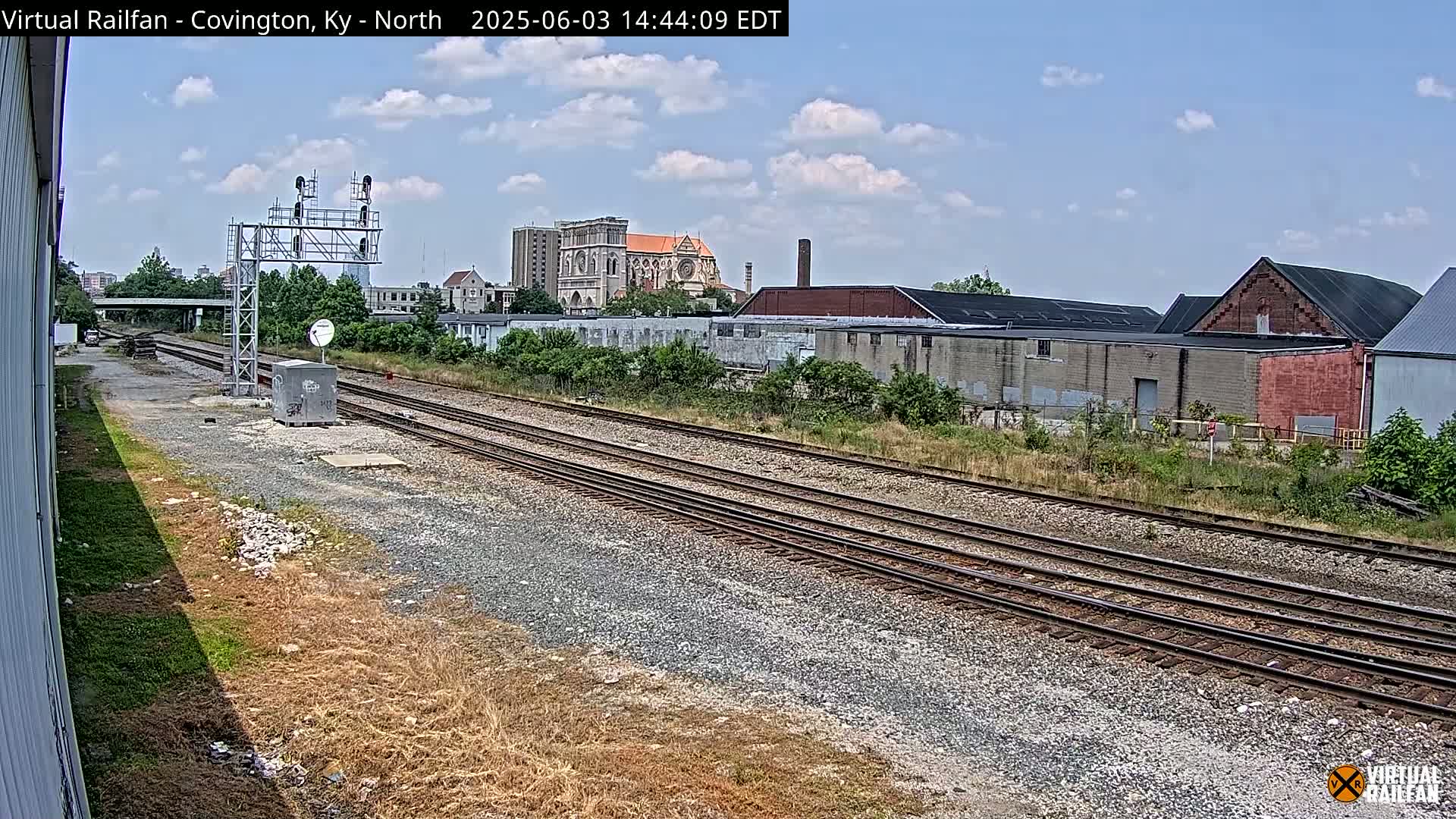 Multiple sets of train tracks stretch into the distance under a partly cloudy sky, past industrial buildings and a church.