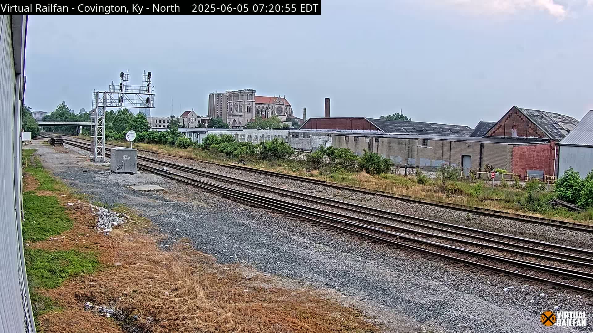 A view of train tracks on a partly cloudy day, with industrial buildings and a large church visible in the background.