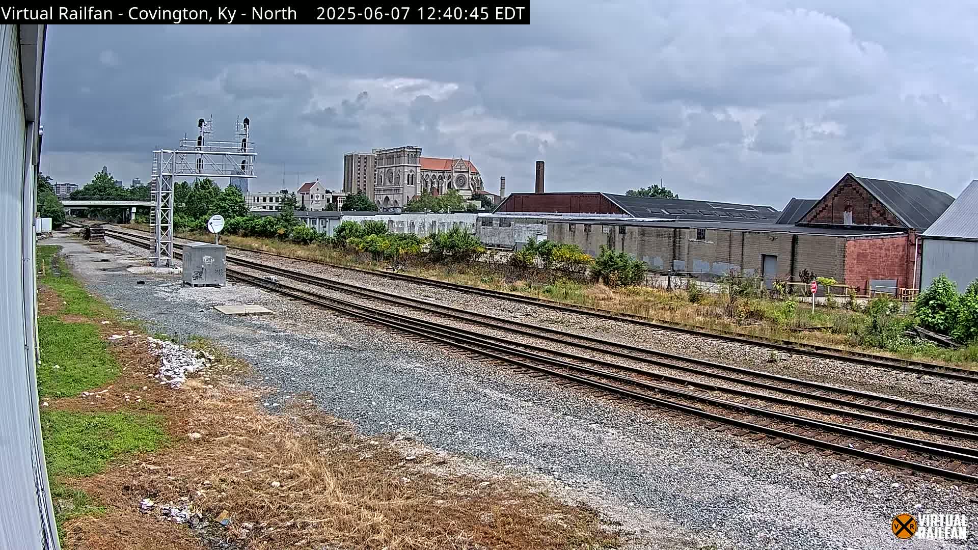 Multiple sets of train tracks stretch towards a large brick building and a church under a cloudy sky.