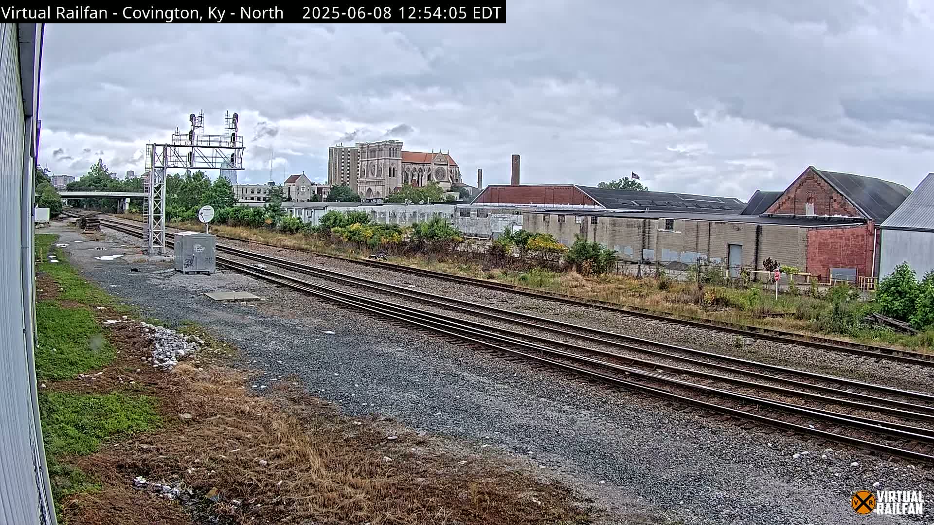 A view of railroad tracks on an overcast day, with industrial buildings and a large cathedral visible in the distance.