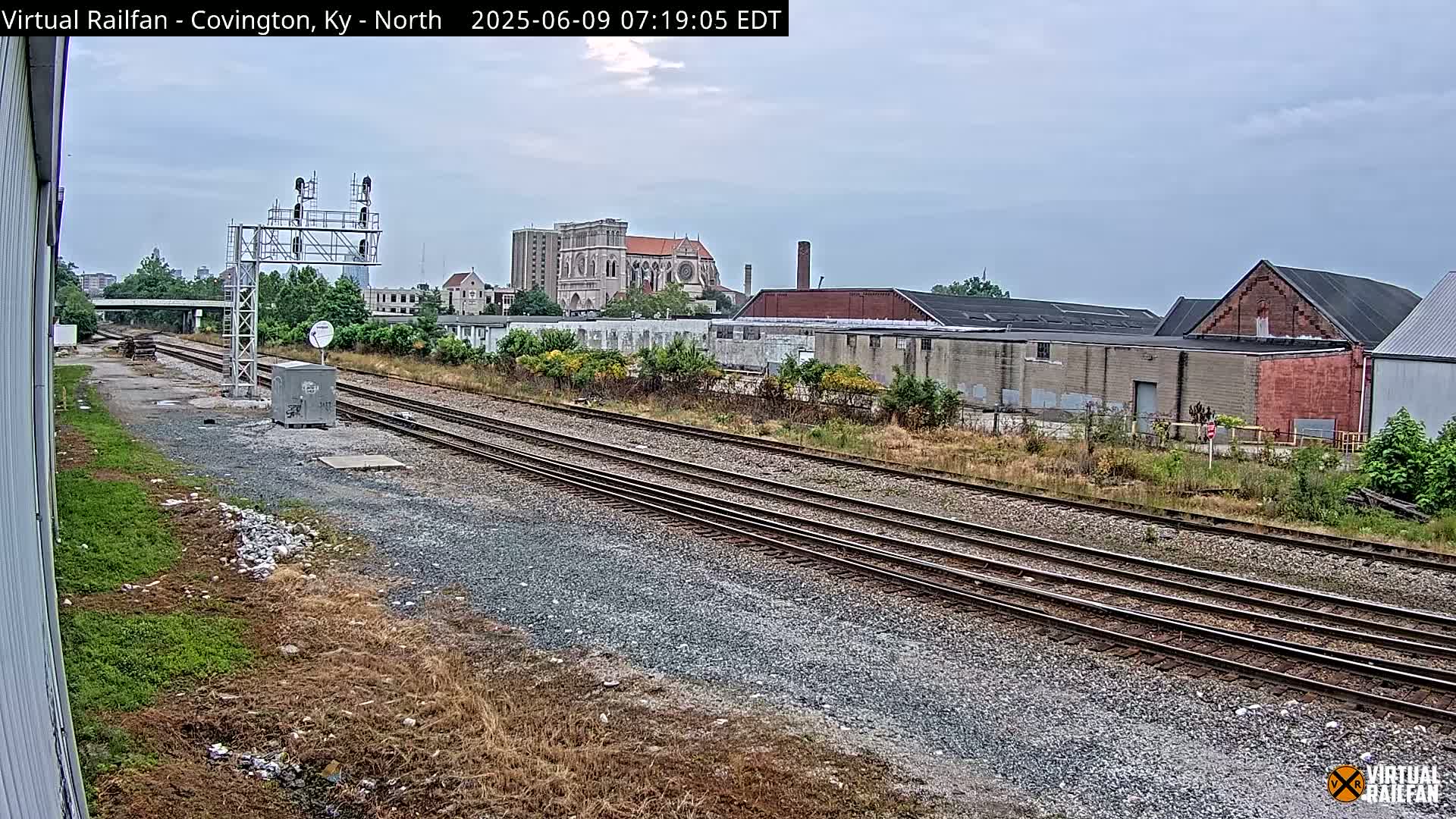 A view of railroad tracks on an overcast day, with industrial buildings and a large church visible in the background.