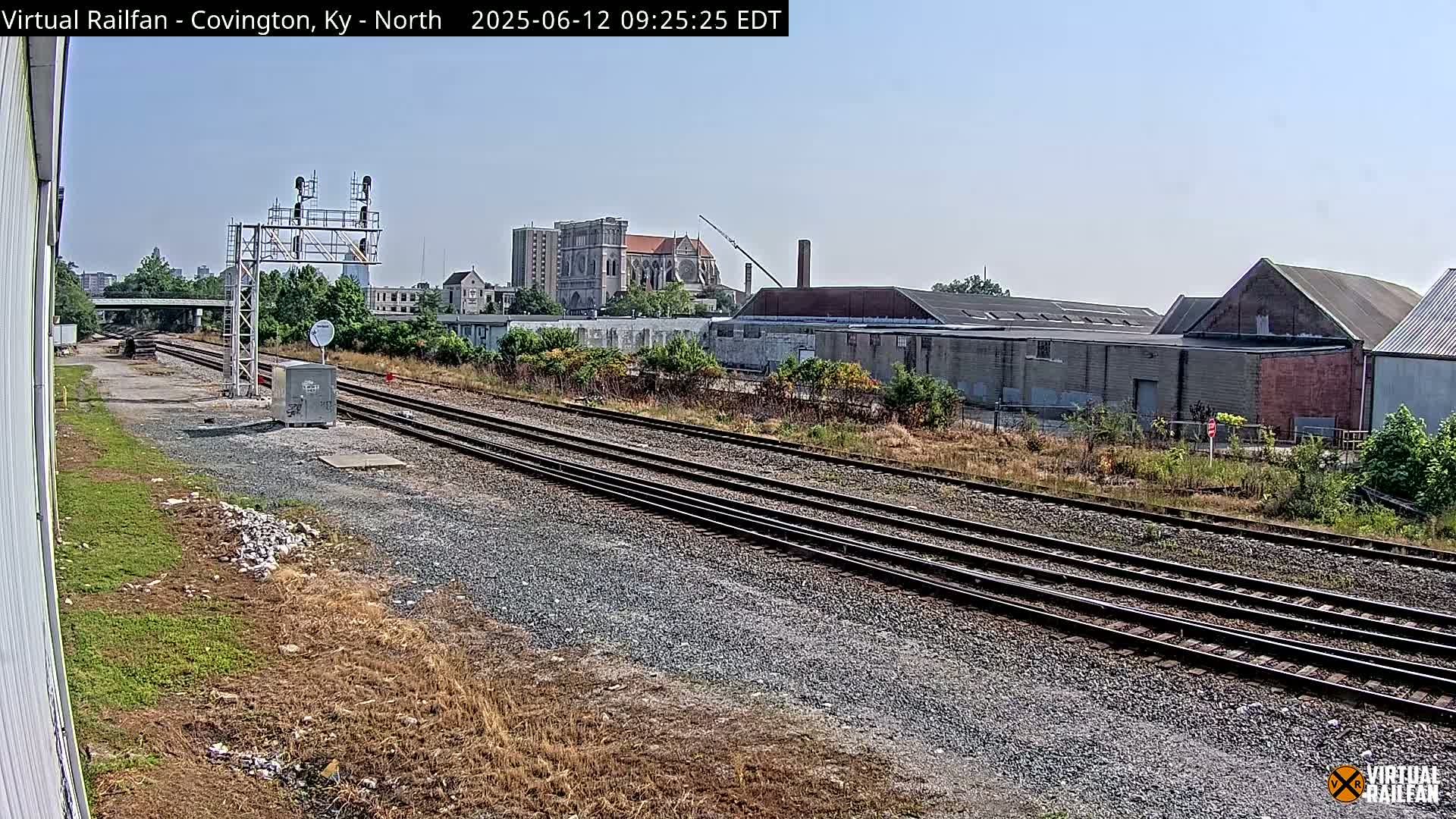 Multiple sets of train tracks extend into the distance under a clear sky, past industrial buildings and a church.