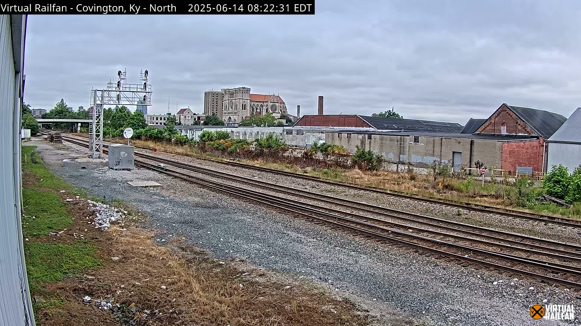 A view of railroad tracks on an overcast day, with industrial buildings and a large church in the background.