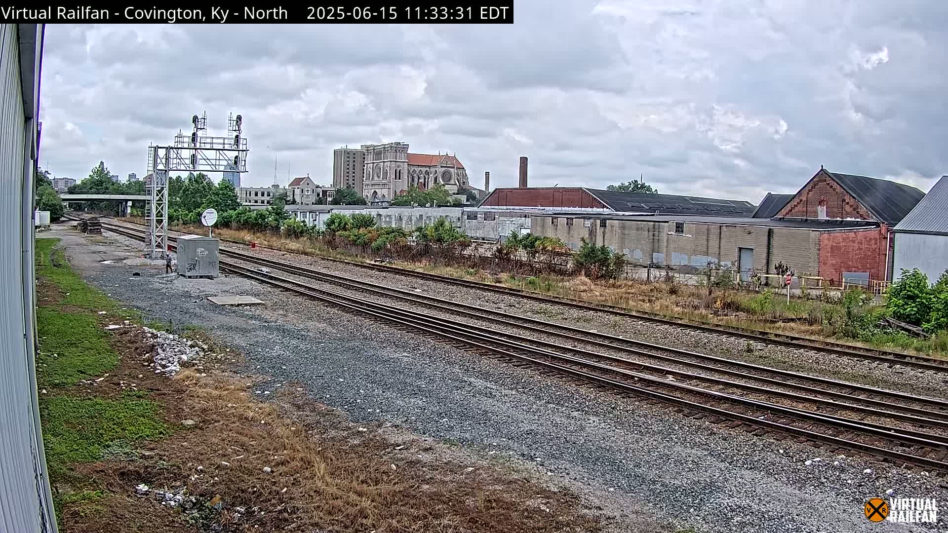 Multiple sets of train tracks run through a gravel area towards a city skyline under a cloudy sky.