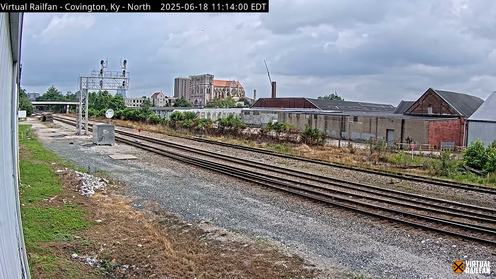 Multiple sets of train tracks extend into the distance under an overcast sky, passing industrial buildings and a church in the background.
