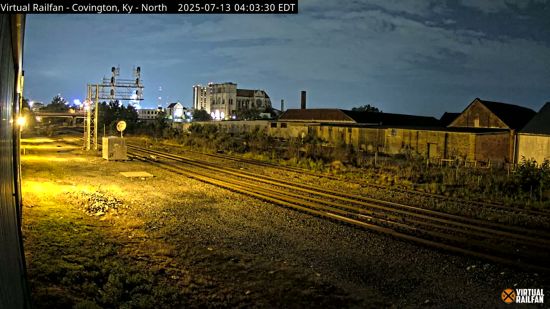 Nighttime view of railroad tracks leading towards buildings under a partly cloudy sky.