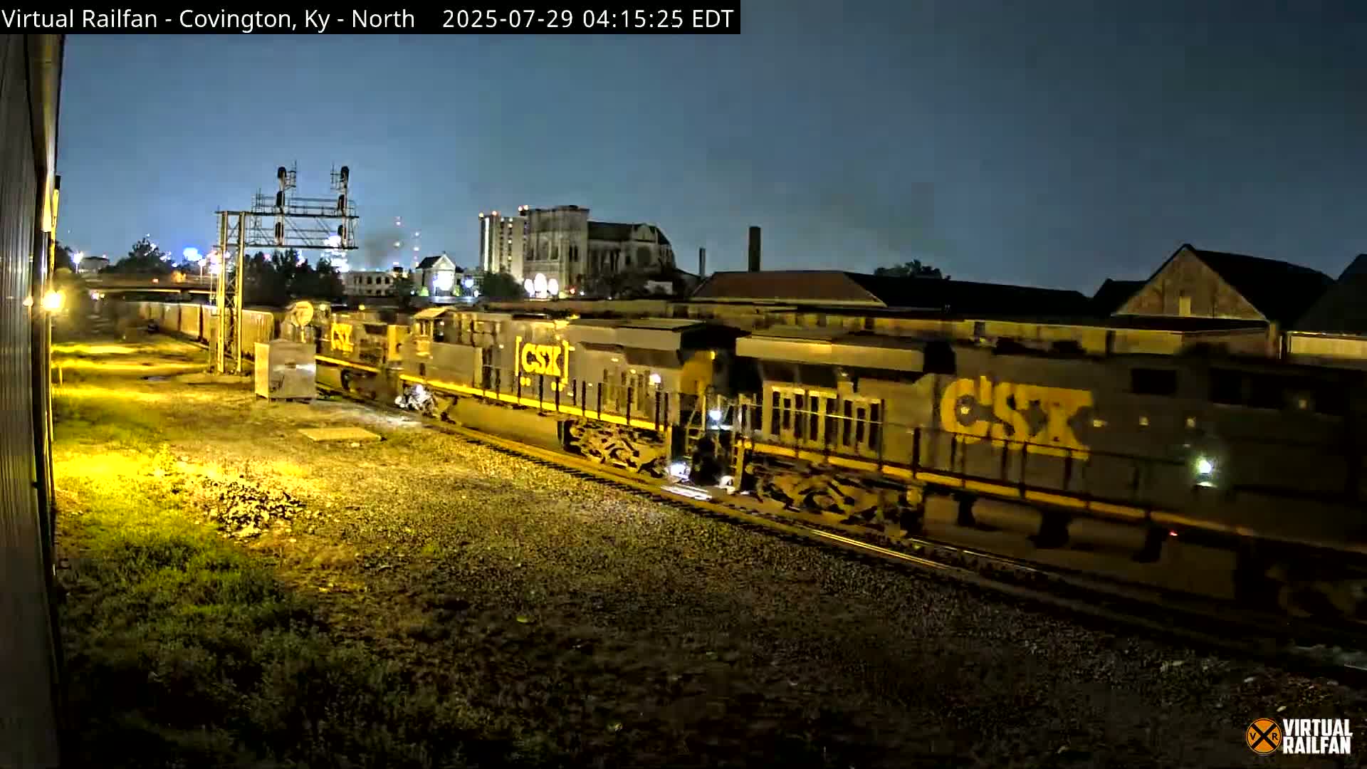 A CSX freight train moves along the tracks at night under a dark, clear sky.