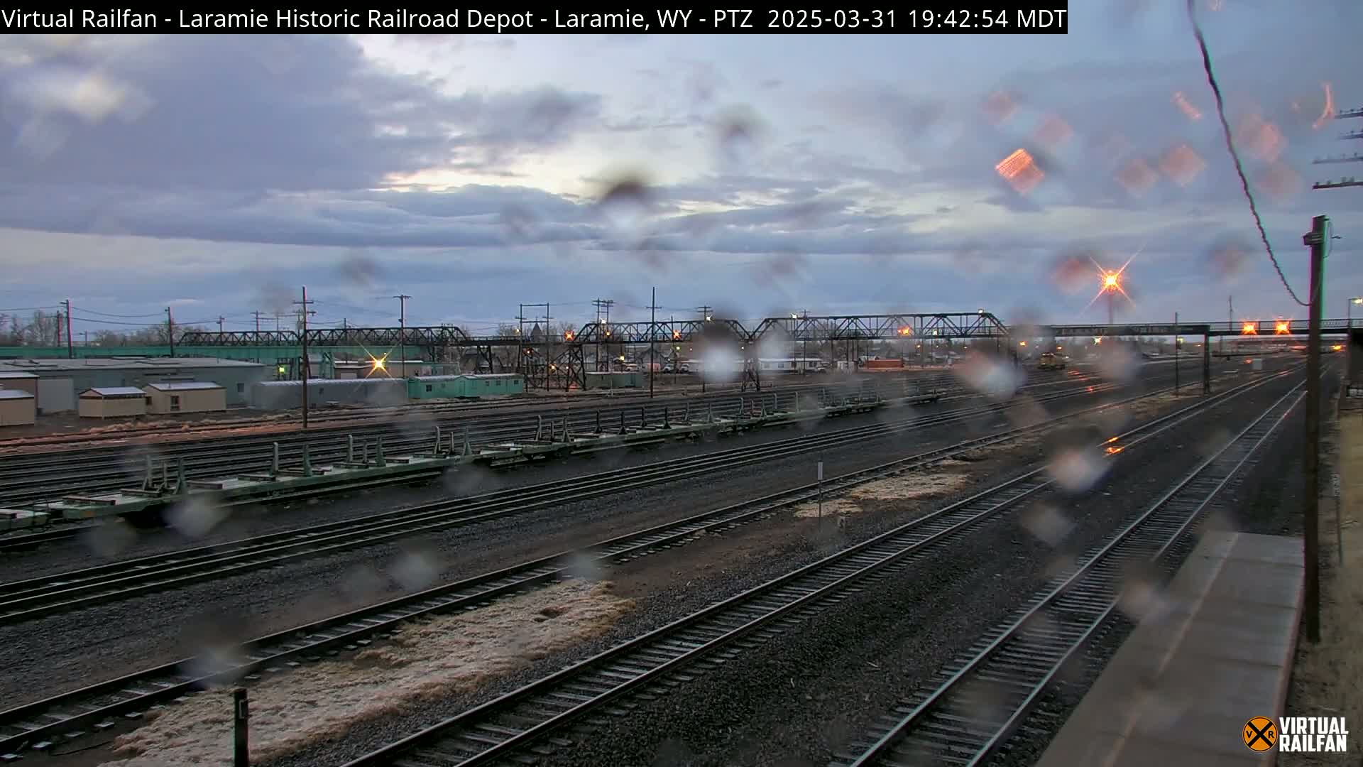 A view of multiple train tracks and railway cars under an overcast sky with rain on the camera lens.