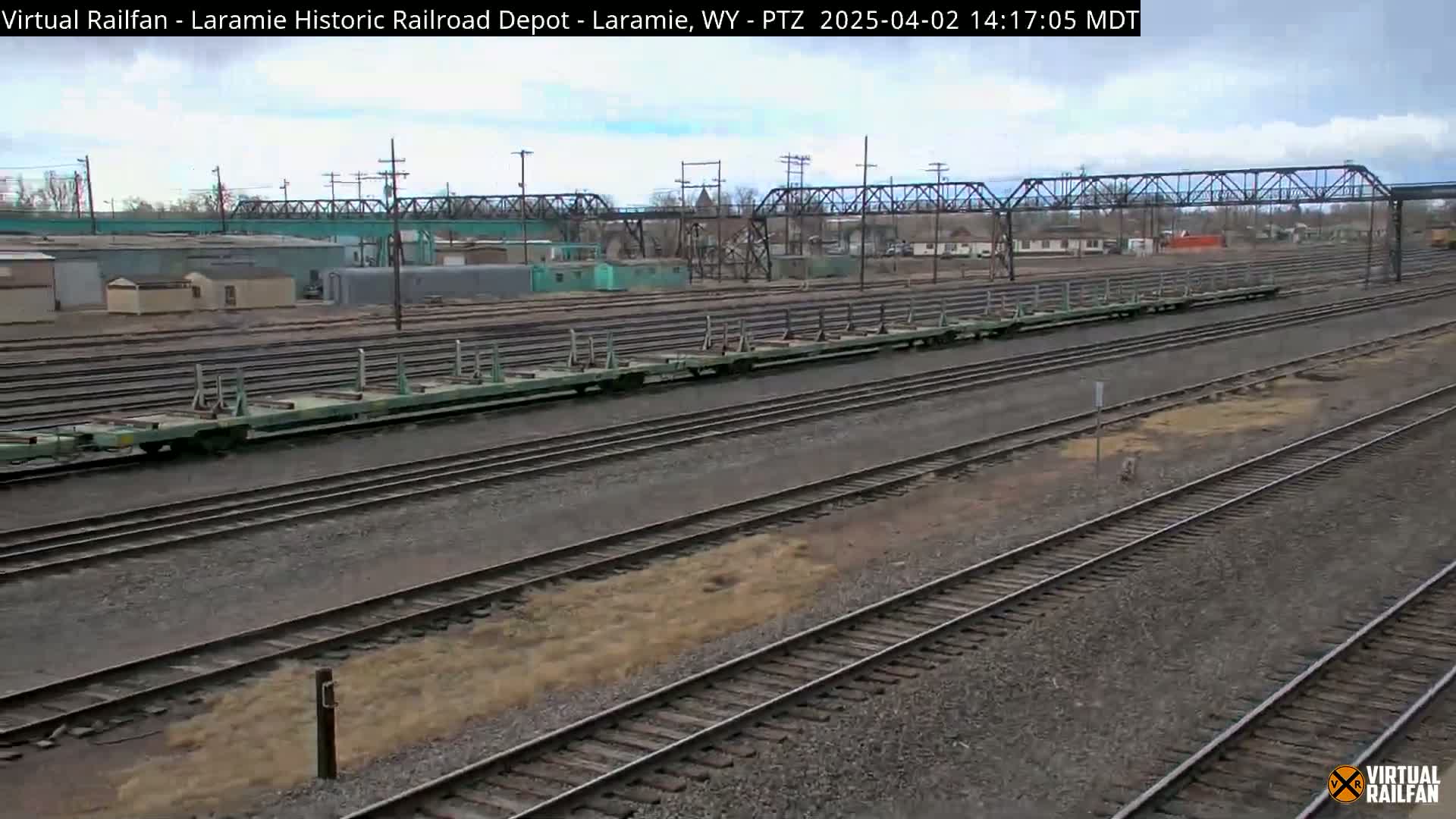 A long, light-green freight train sits on a set of railway tracks in an overcast outdoor setting.