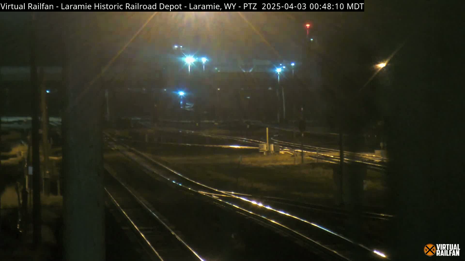 A nighttime view of a railroad yard with several sets of tracks illuminated by artificial lights in foggy conditions.