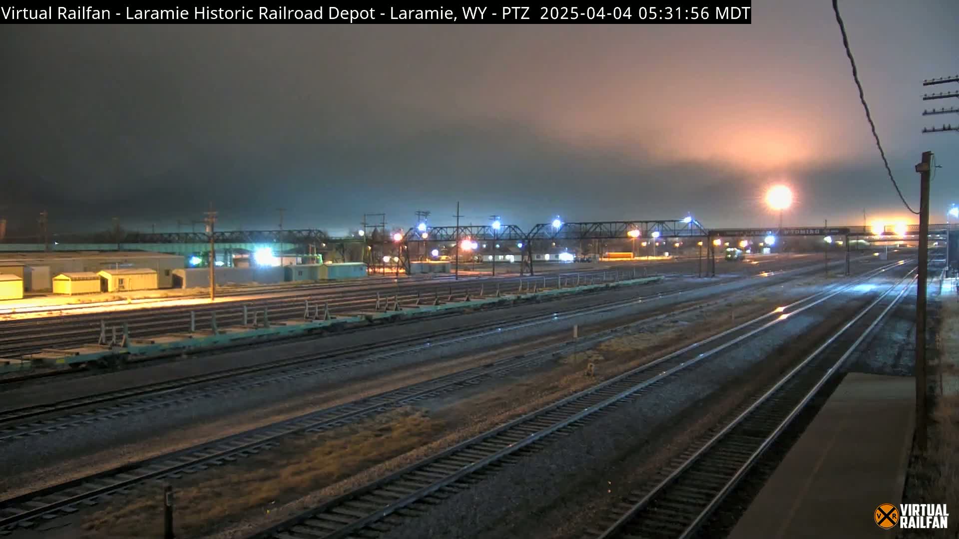 A nighttime view of a railroad yard with several train cars, illuminated by lights under a dark, cloudy sky.
