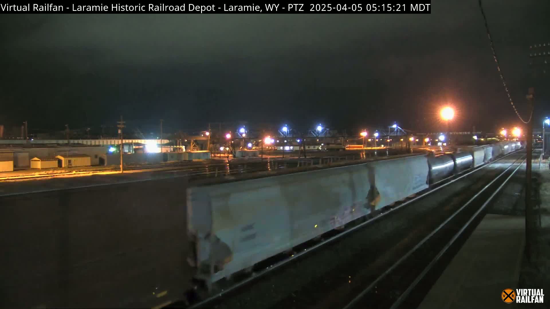 A long freight train moves through a dimly lit rail yard at night.