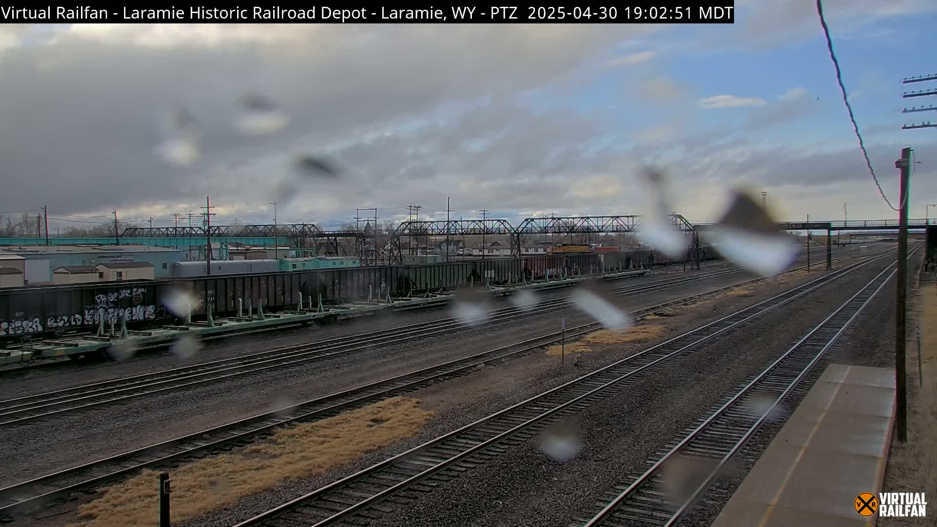 A view of railroad tracks and freight cars on an overcast day with rain on the camera lens.