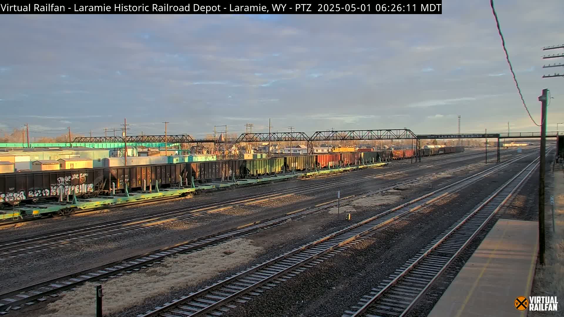 A long freight train sits on a rail yard under a partly cloudy sky.