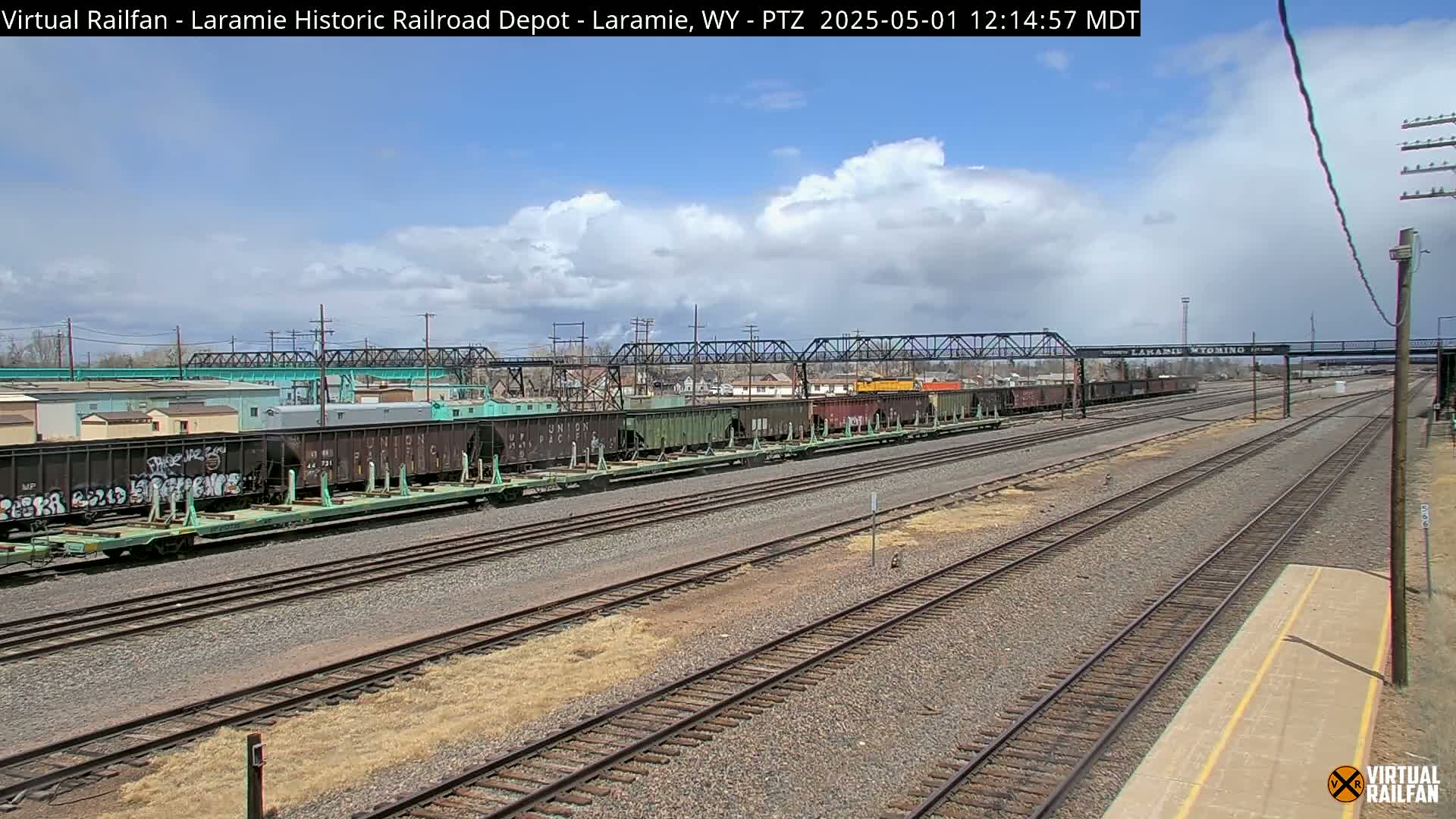 A long freight train sits on a railway under a partly cloudy sky.