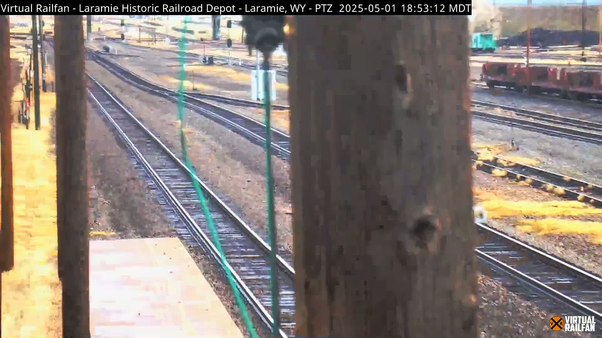 Multiple sets of train tracks stretch into the distance on a sunny day, with a wooden post partially obscuring the view.