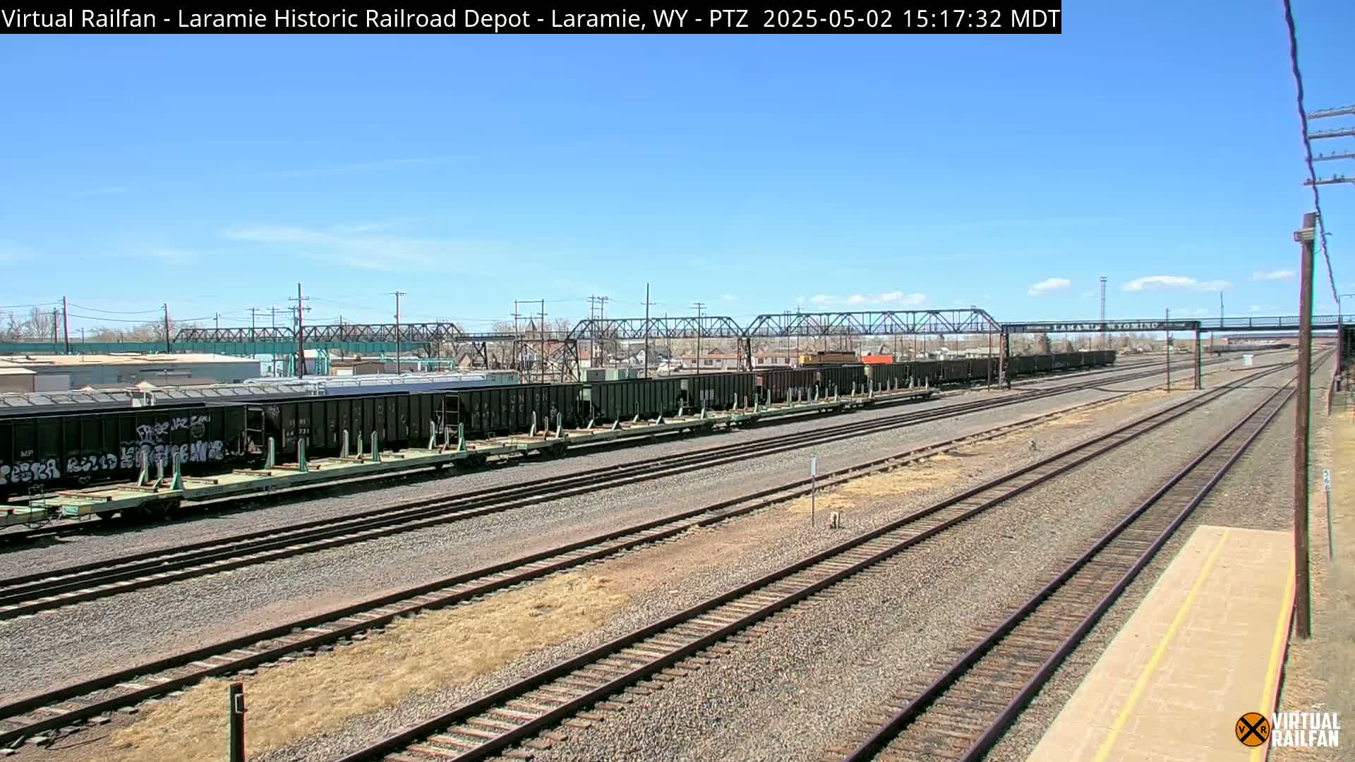 A long freight train sits on multiple railway tracks under a clear blue sky.
