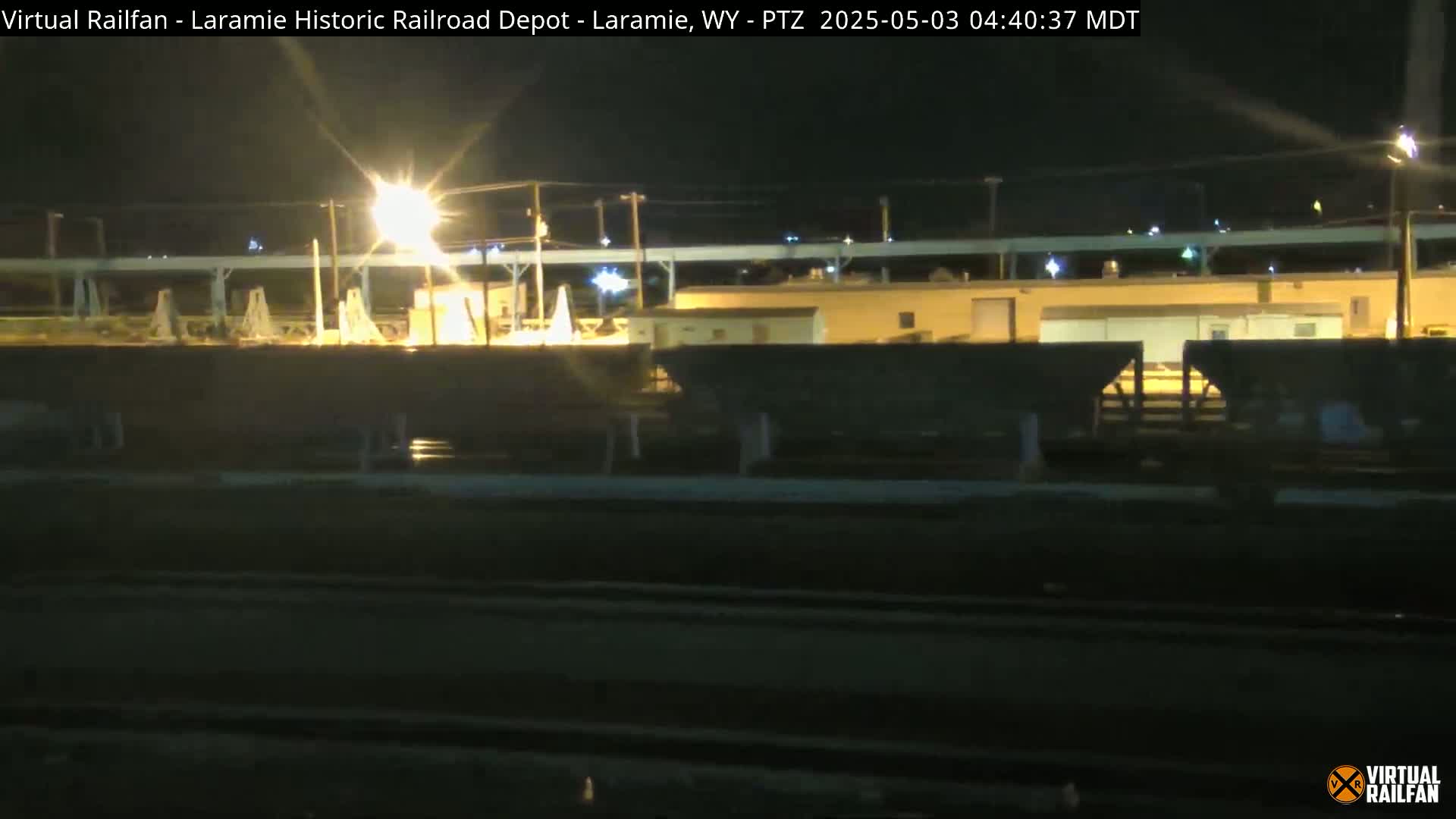 A nighttime view of a railroad yard with several dark freight cars under bright lights.