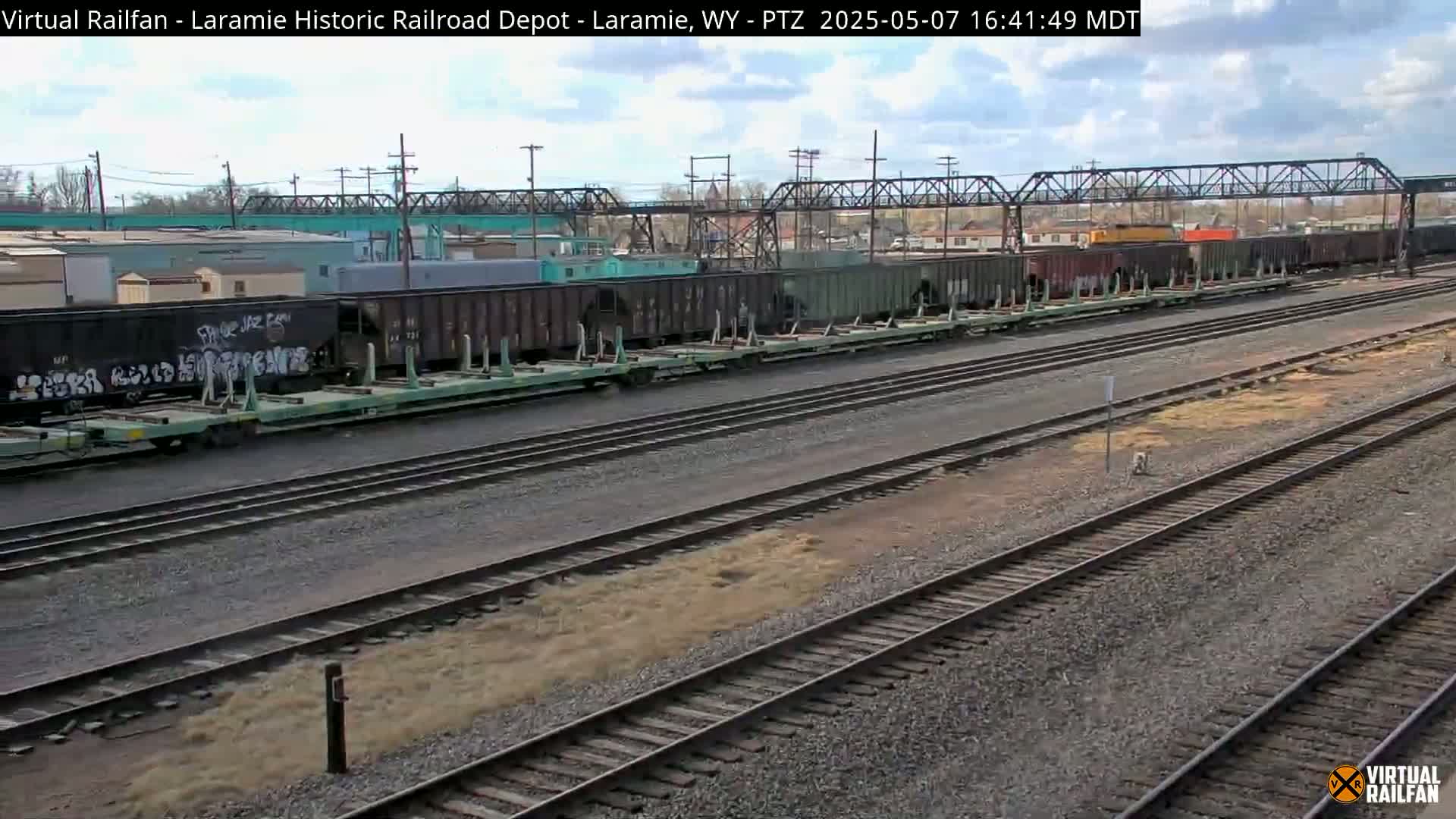A long freight train sits on a rail yard under a partly cloudy sky.
