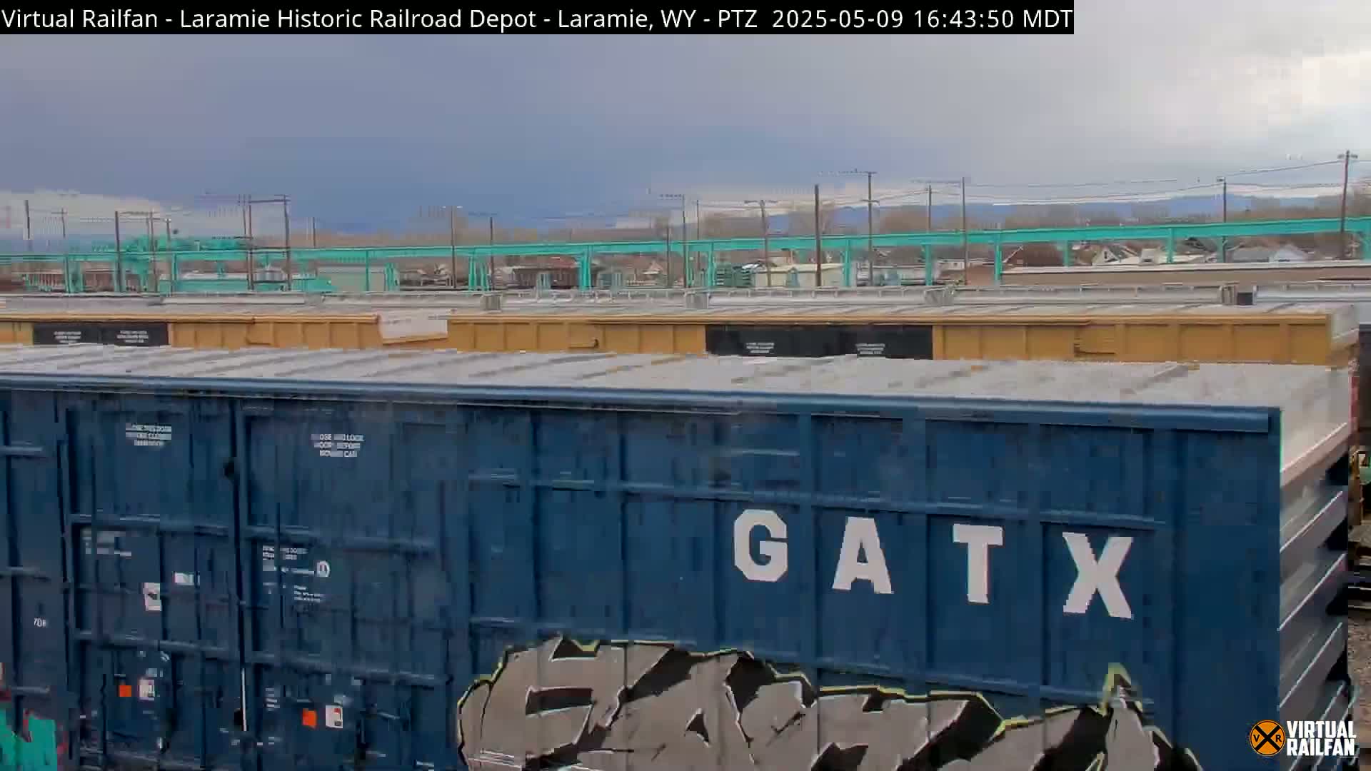 A view of several dark-blue and tan freight train cars under an overcast sky.