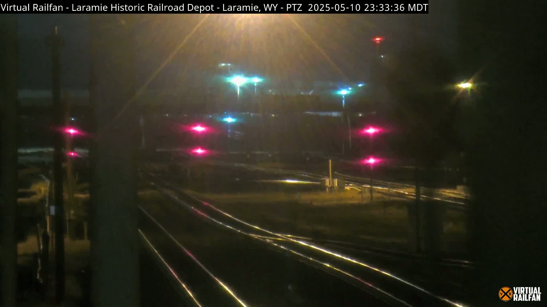 A nighttime view of railroad tracks and signals, illuminated by various colored lights.