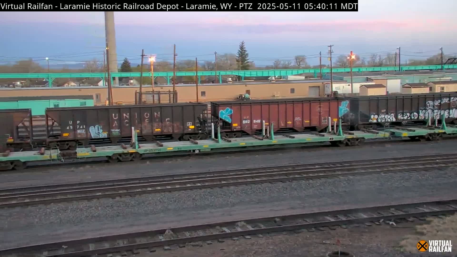Several graffiti-covered rail cars sit on railroad tracks at dawn under a pale sky.