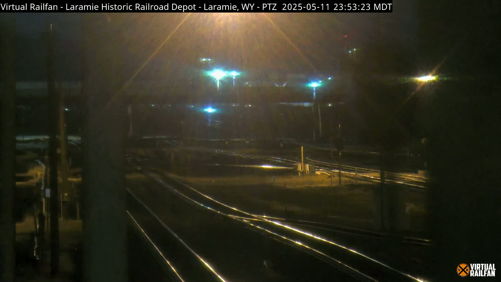 At night, a view of a railroad yard with several sets of tracks, illuminated by bright lights under a dark, possibly overcast sky.