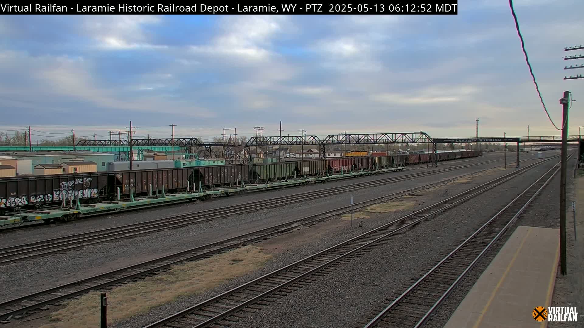A long freight train sits on a rail yard under a partly cloudy sky.