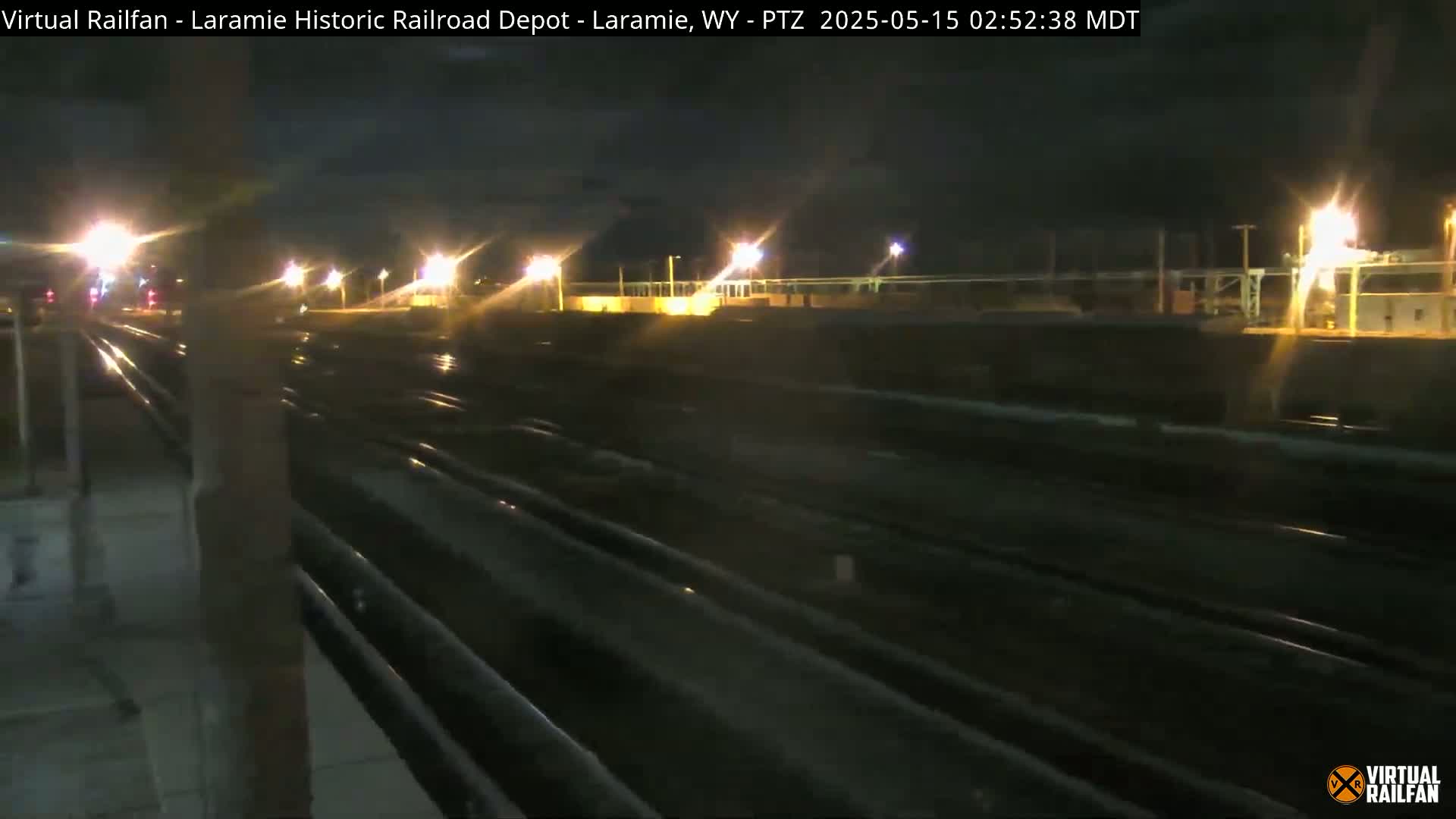 A nighttime view of a railroad yard with multiple tracks extending into the distance under slightly overcast skies.