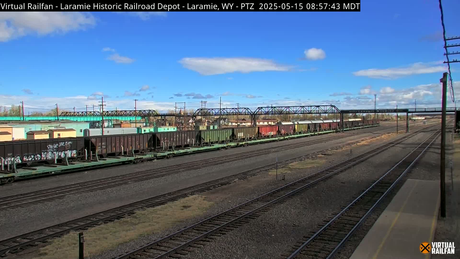 A long freight train sits on a rail yard under a mostly sunny sky.