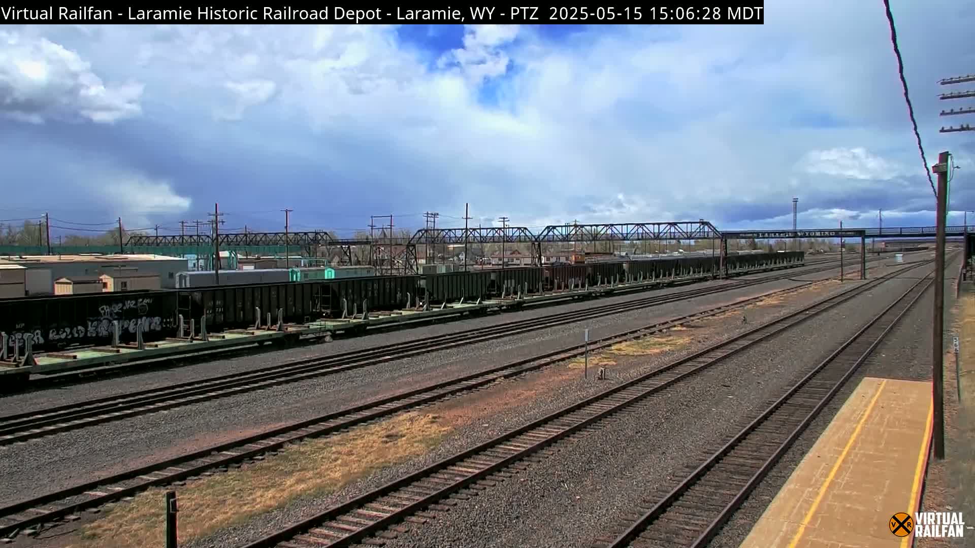 A long line of freight cars sits on a railway under a partly cloudy sky.