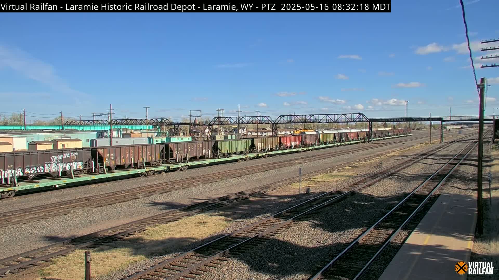 A long freight train sits on a railway track under a mostly clear blue sky.