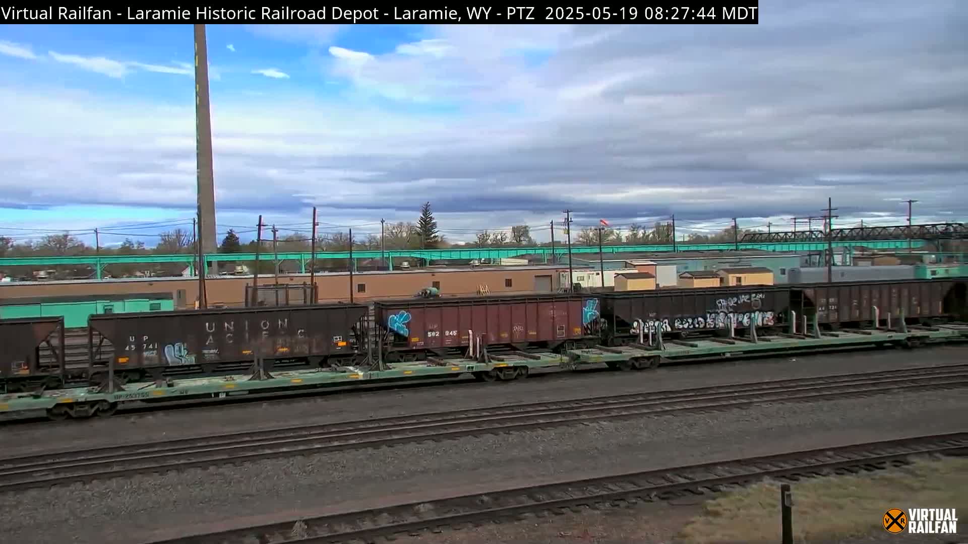 A long line of graffiti-covered train cars sits on railroad tracks under a partly cloudy sky.