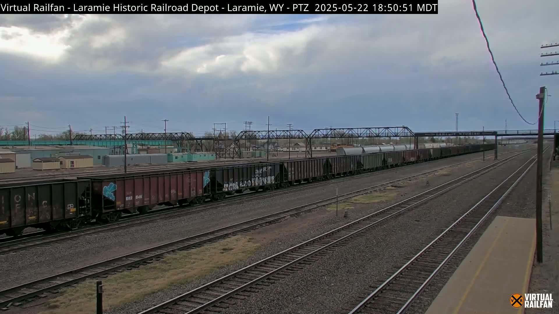 A long freight train sits on railroad tracks under a cloudy sky.