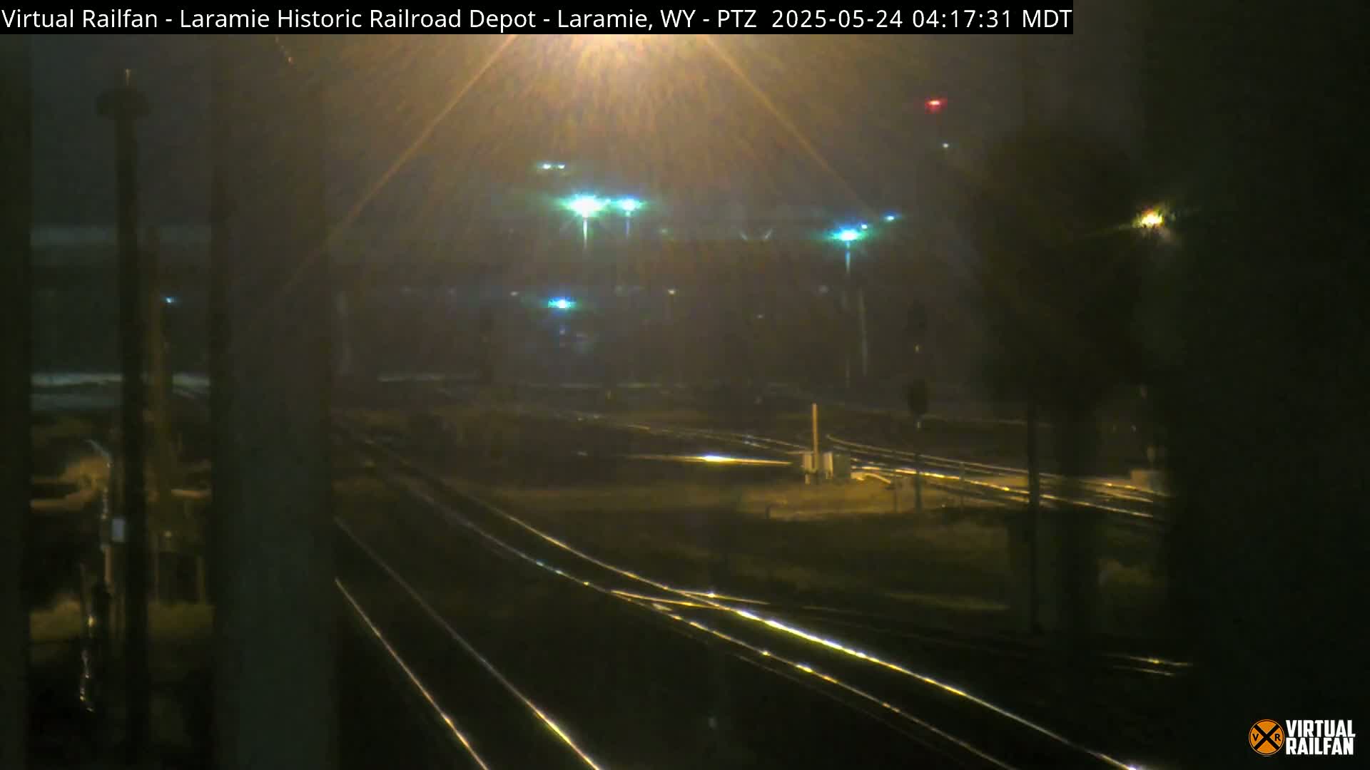 A nighttime view of a railroad yard shrouded in fog or mist, illuminated by several lights.