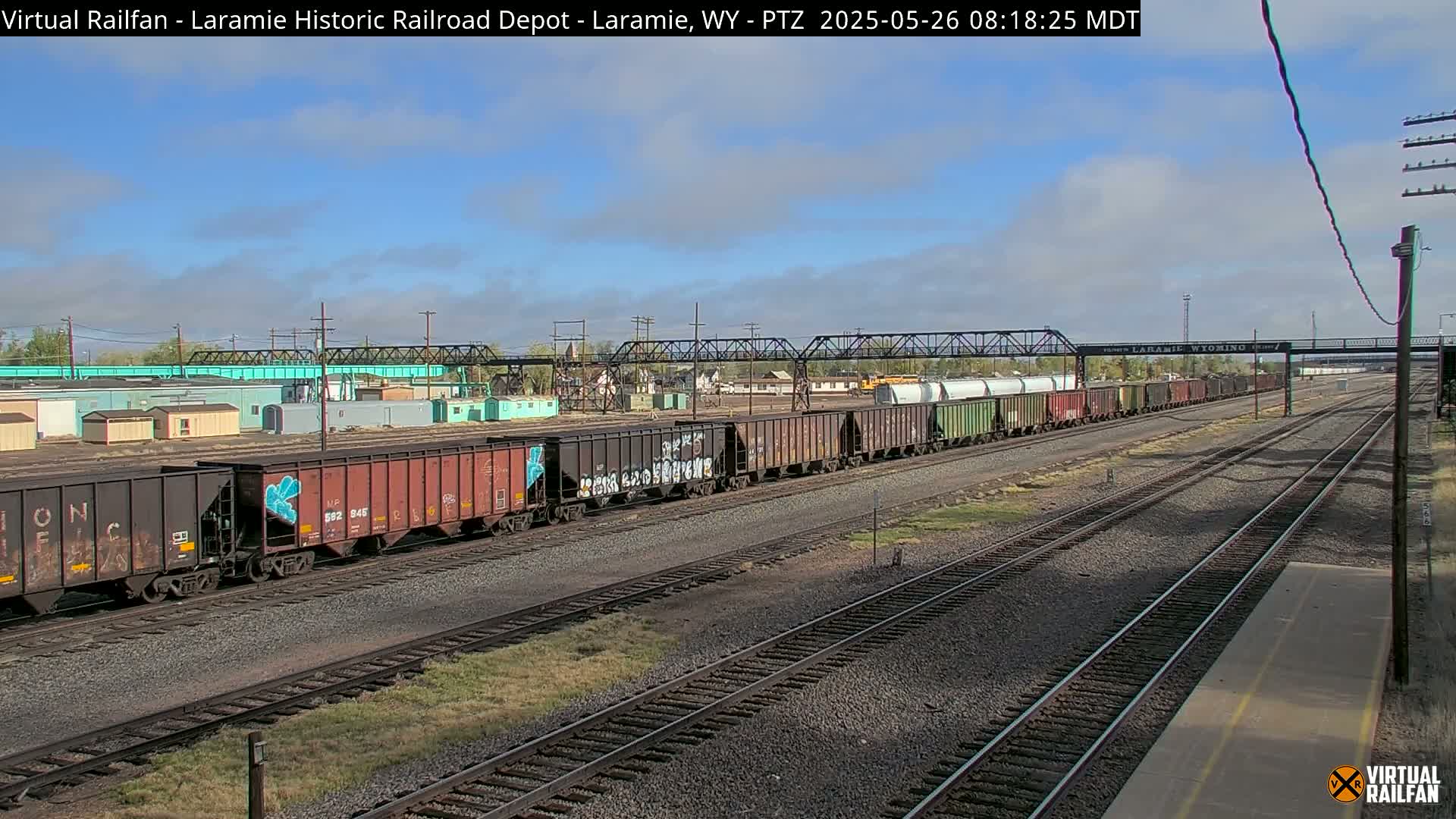A long freight train sits on a railway under a partly cloudy sky.