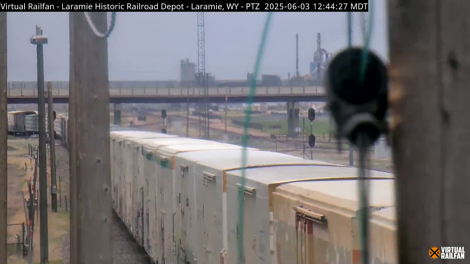 A long freight train of light-colored boxcars moves past under an overcast sky.