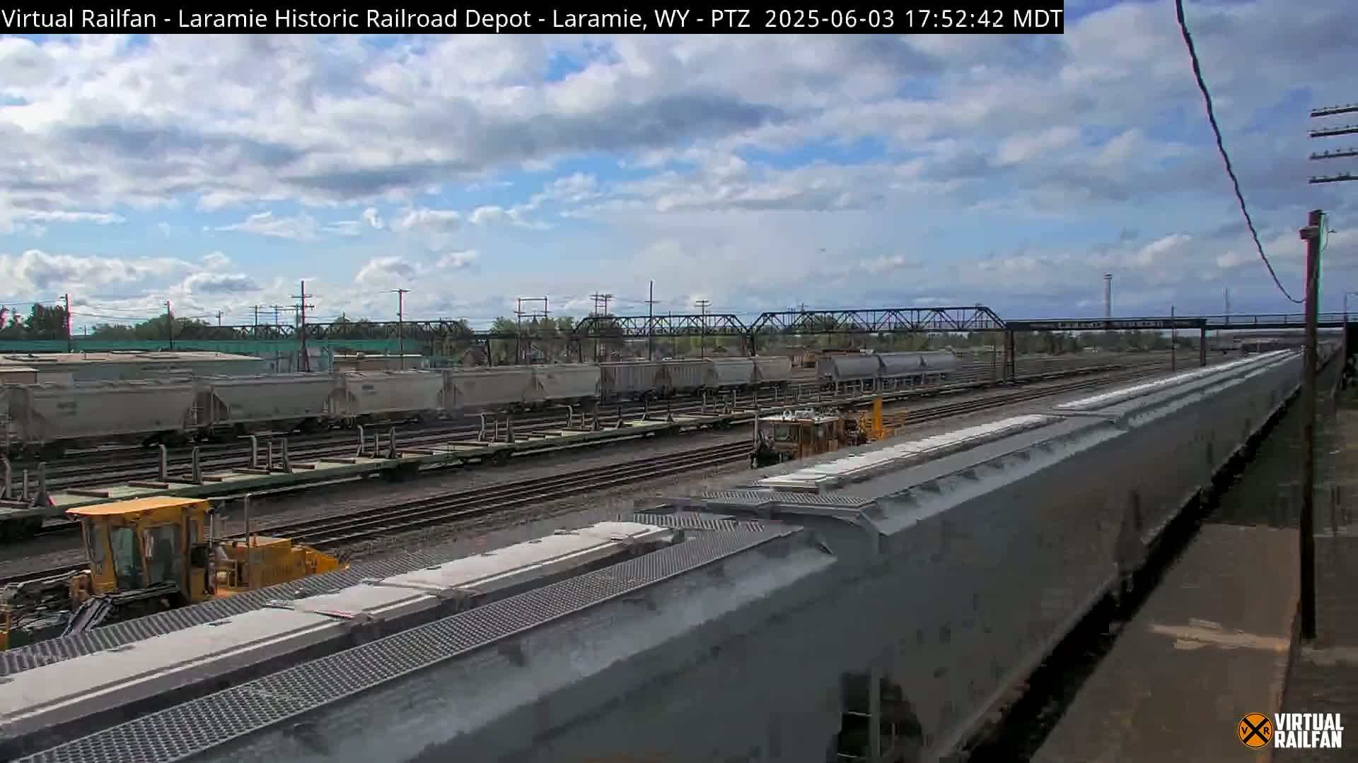 A mostly cloudy sky overlooks a railroad yard with several long freight trains and railway maintenance equipment.