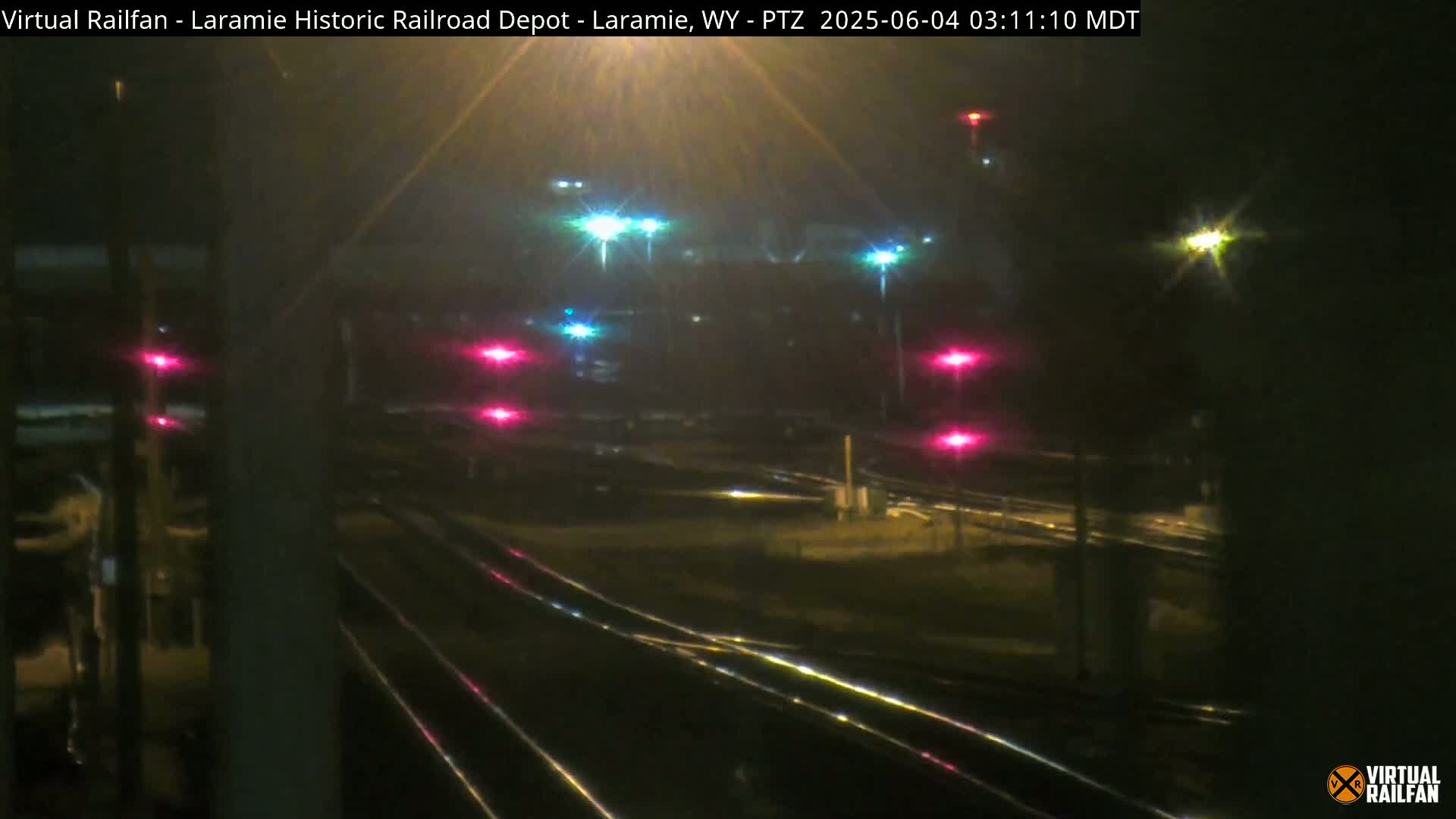 A nighttime view of railroad tracks and signals, illuminated by various lights.