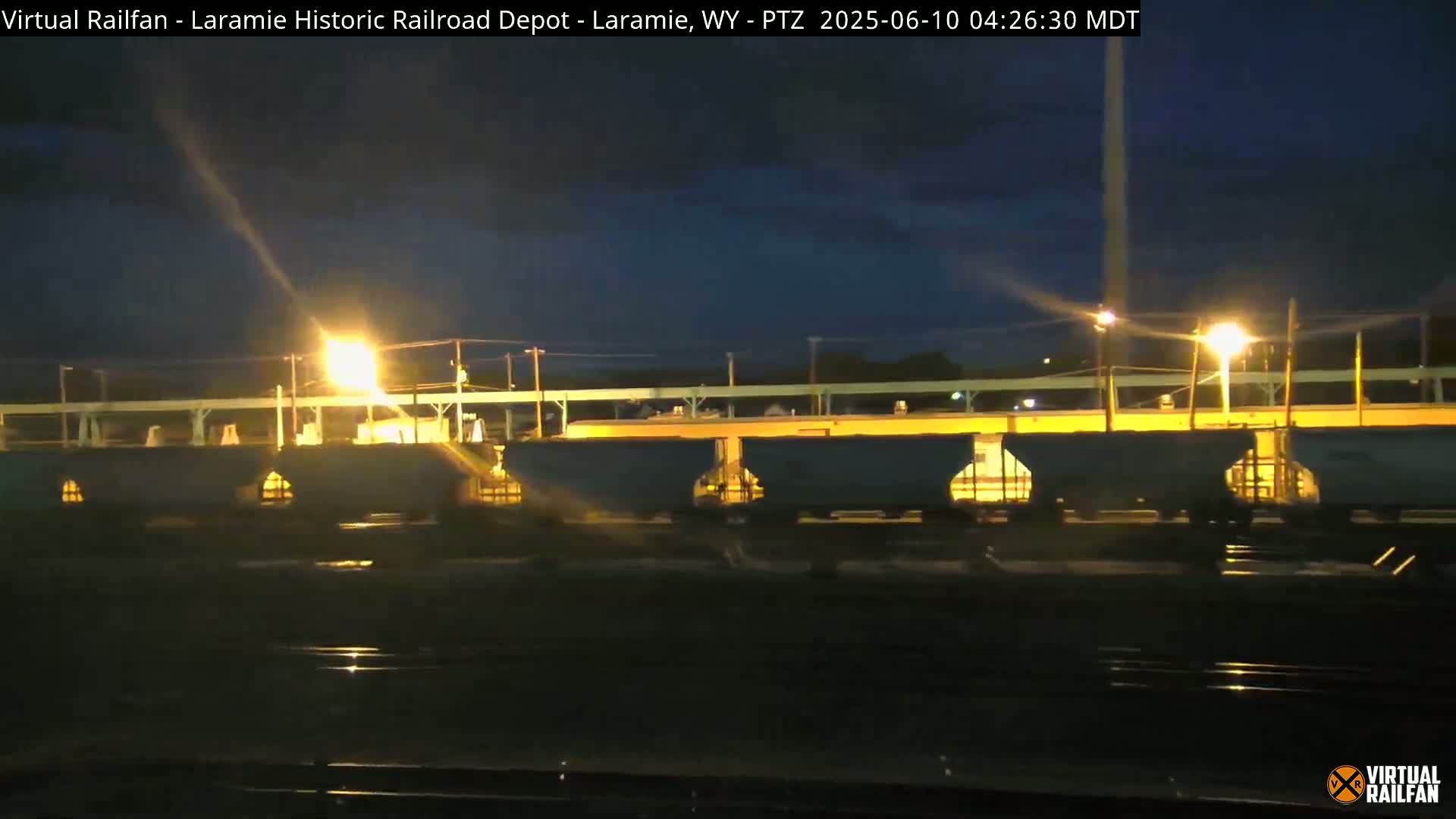 Under a dark night sky, a line of illuminated rail cars sits stationary on a track.