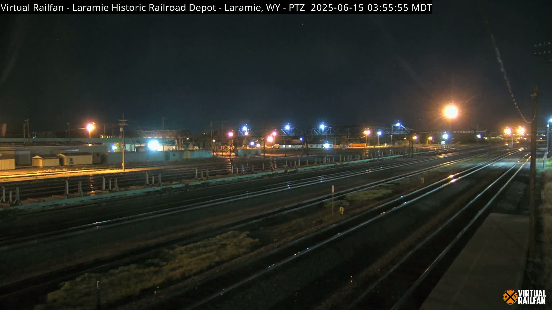 A nighttime view of a railroad yard with multiple sets of tracks, illuminated by artificial lights under a clear, dark sky.
