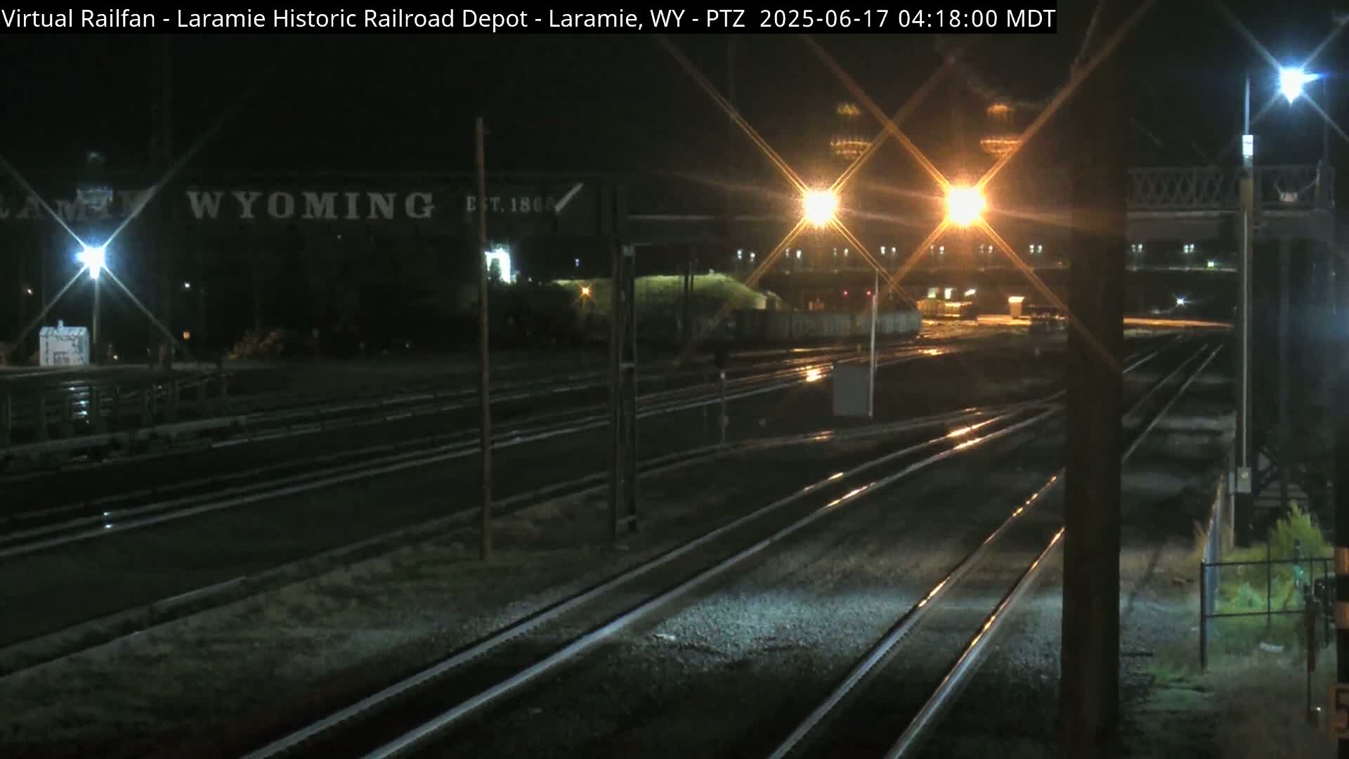 At night, several sets of train tracks stretch into the distance under bright lights, with a sign reading "WYOMING" visible in the background.